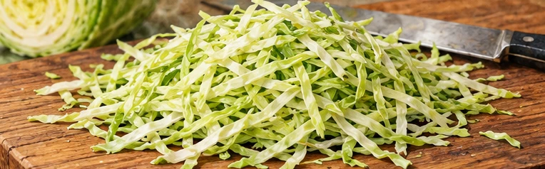Fine ribbons of raw green cabbage on a cutting board